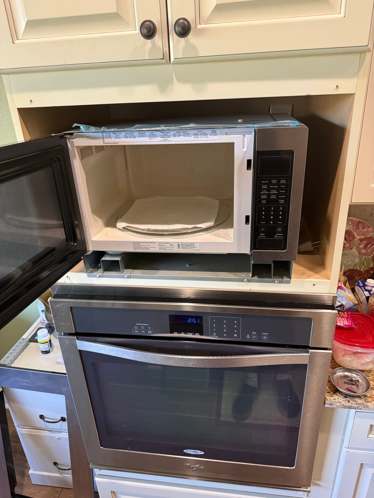 Empty cabinet opening above the wall oven with the Whirlpool microwave pulled halfway out and its door open