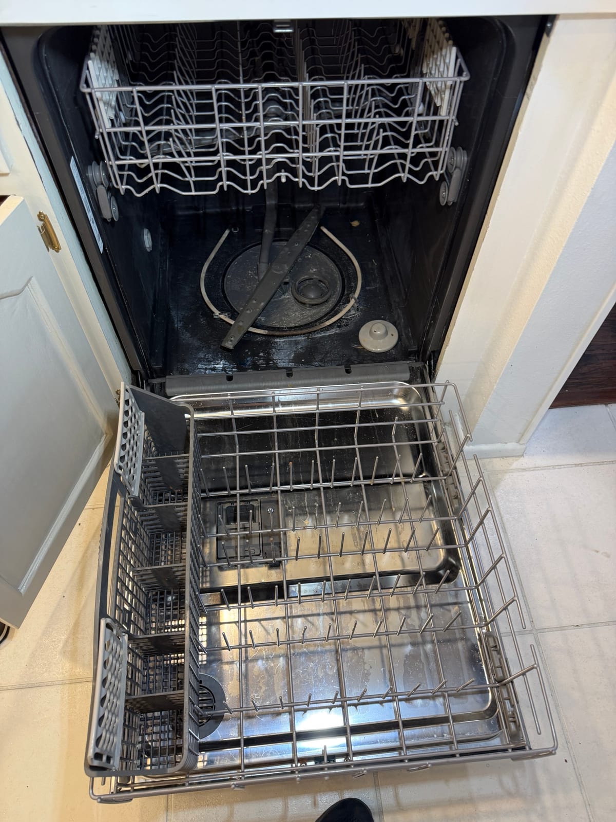 Whirlpool dishwasher open with the racks pulled out, showing a dark stained tub