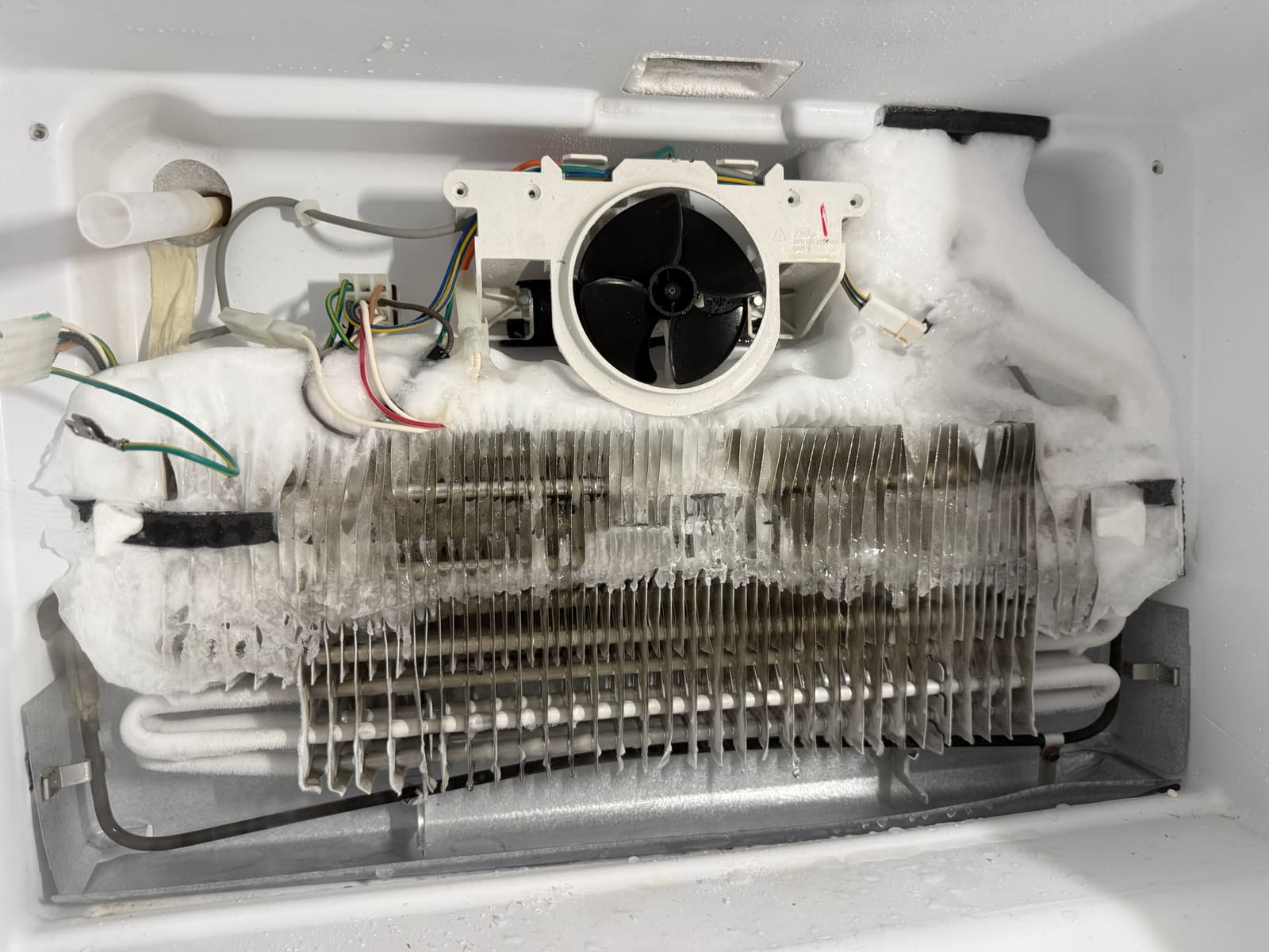 Whirlpool freezer evaporator coil covered in thick ice, with ice reaching the fan housing