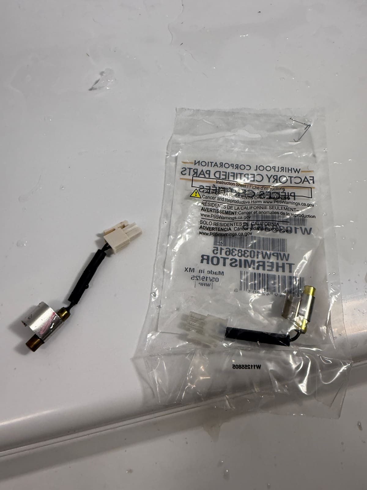 Old defrost thermistor next to a new Whirlpool factory certified thermistor in its bag