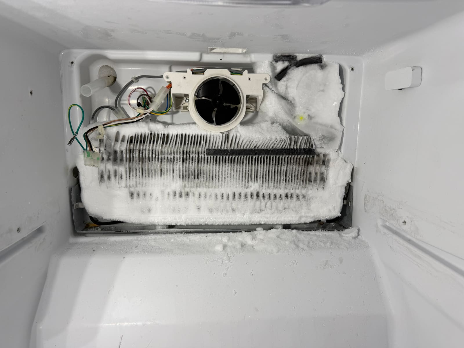 Whirlpool freezer with the back panel off, showing the evaporator coil covered in ice and frost built up around the fan, in East Lake Landing, Palm Harbor