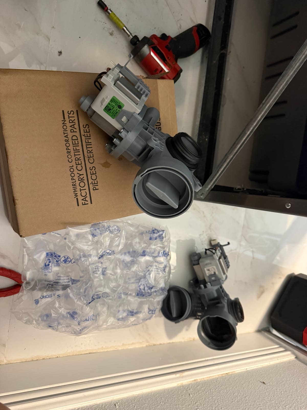 New Whirlpool drain pump on its parts box, with the old drain pump below it