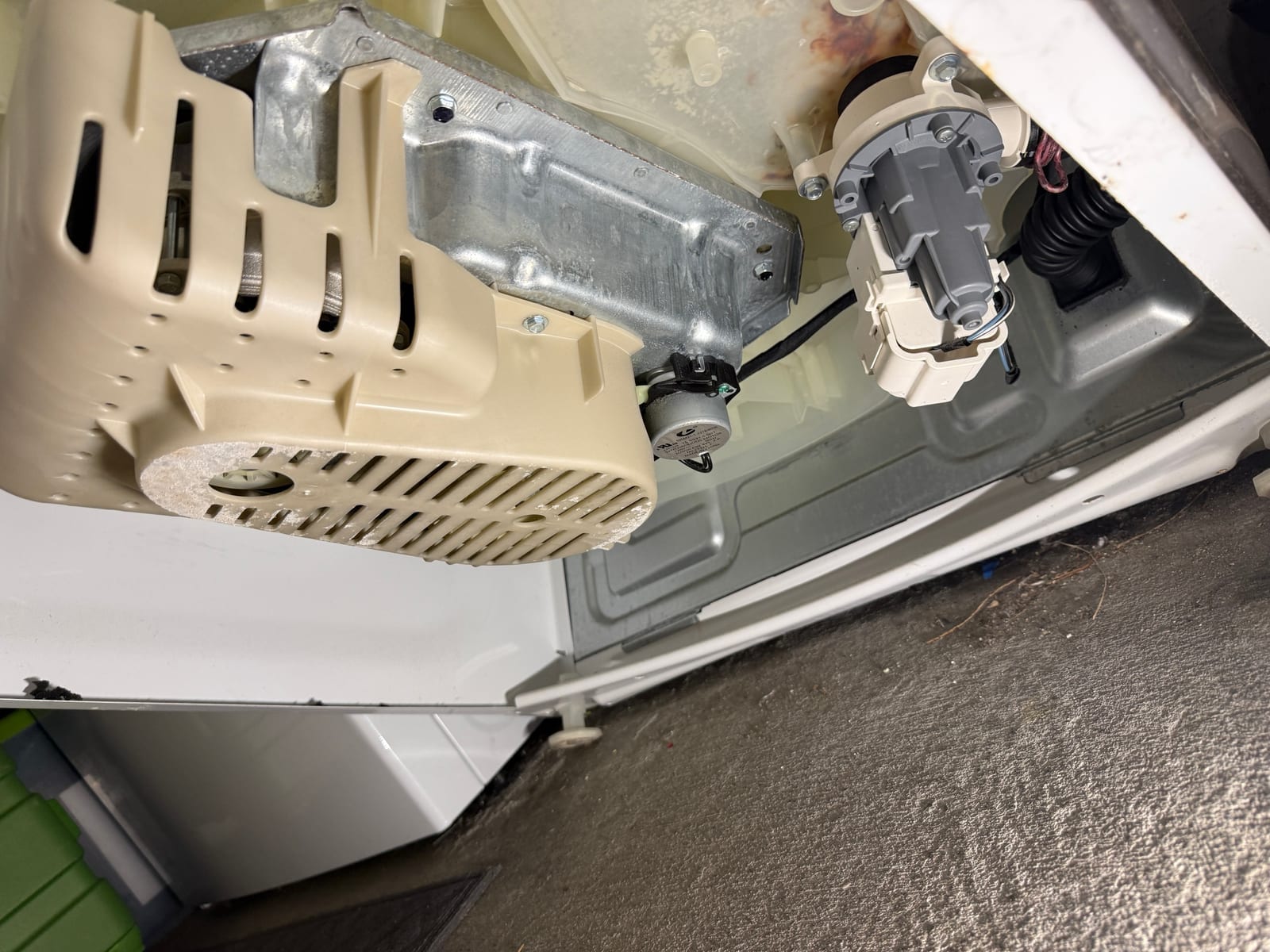 Whirlpool top-load washer laid back to reach underneath, showing the motor housing, the drain pump and the rubber hose